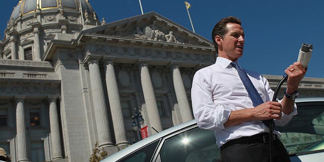 California Gov. Gavin Newsom holds a power cable before test driving a hybrid Toyota Prius when he was mayor of San Francisco.