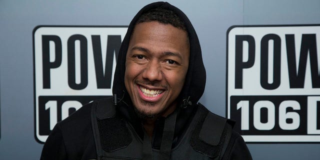 Nick Cannon smiles in a black hooded sweatshirt and vest