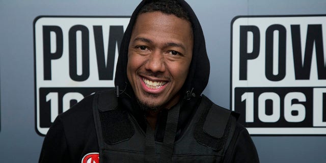 Nick Cannon smiles in a black hooded sweatshirt and vest