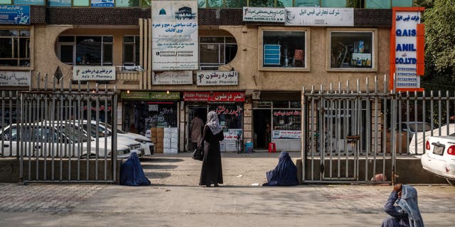 A pedestrian stands beside begging women as they wait to cross a street in front of a wholesale pharmaceutical market in Kabul, Afghanistan, July 12, 2020.