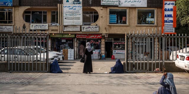 A pedestrian stands beside begging women as they wait to cross a street in front of a wholesale pharmaceutical market in Kabul, Afghanistan, July 12, 2020.