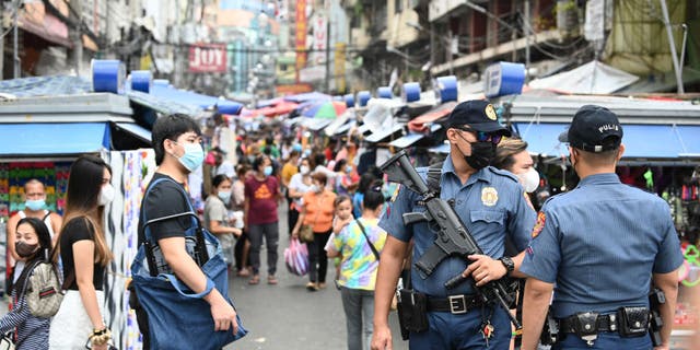 A policeman carrying an automatic rifle stands guard with a colleague along a popular market street in Manila, Philippines, on June 1, 2022.