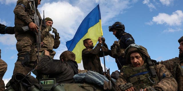 Ukrainian soldiers adjust a national flag atop an armored personnel carrier on a road near Lyman, Donetsk region on Oct. 4, 2022.