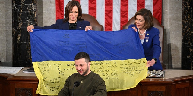 Ukraine's President Volodymyr Zelensky addresses the US Congress as US Vice President Kamala Harris and US House Speaker Nancy Pelosi, D-Calif., hold a Ukrainian national flag that Zelensky gave them at the US Capitol in Washington, DC on December 21, 2022.