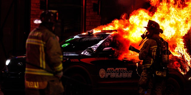 Firefighters work to extinguish a fire after an Atlanta police vehicle was set on fire during a "Stop cop city" protest in Atlanta, Georgia, United States on January 21, 2023. Multiple buildings were vandalized and an Atlanta police vehicle was set on fire as multiple arrests were made.