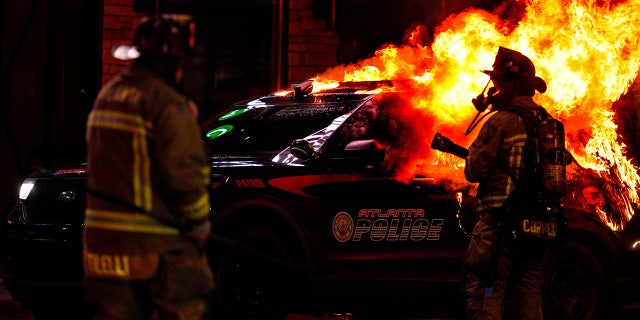 Firefighters work to extinguish a fire after an Atlanta police vehicle was set on fire during a "Stop cop city" protest in Atlanta, Georgia, United States on January 21, 2023. Multiple buildings were vandalized and an Atlanta police vehicle was set on fire as multiple arrests were made.