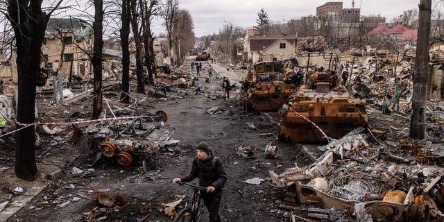 A man pushes his bike through debris and destroyed Russian military vehicles on a street in Bucha, Ukraine.