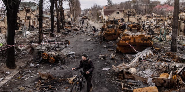 A man pushes his bike through debris and destroyed Russian military vehicles on a street in Bucha, Ukraine.