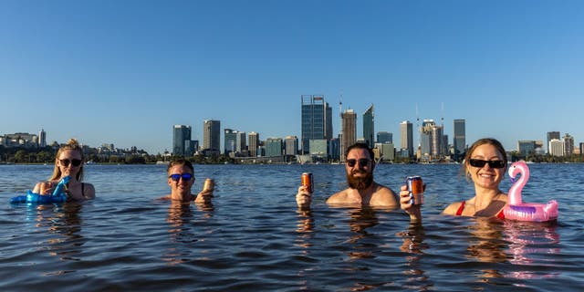 Sarah Jackson, Sam Rowe, Lachlan Alexander and Monica Lewis enjoy a drink and swim in the Swan River at South Perth on January 22, 2022 in Perth, Australia. 