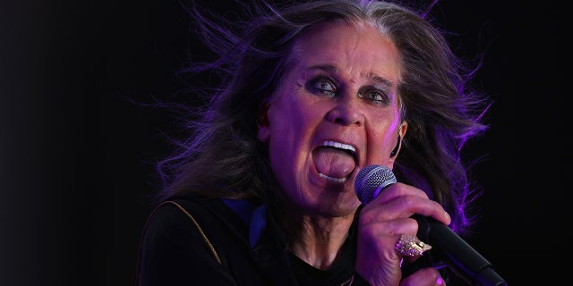 Ozzy Osbourne with thick black eyeliner and long hair blowing in the wind sings into a microphone