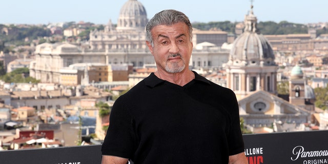 Sylvester Stallone in a black t-shirt with the backdrop of Rome behind him