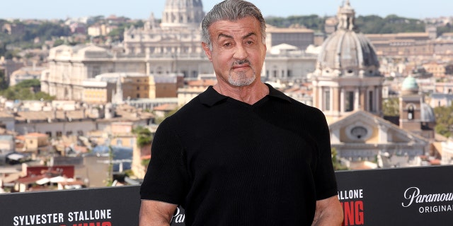 Sylvester Stallone in a black t-shirt with the backdrop of Rome behind him