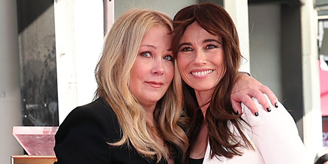 Christina Applegate in black poses on the Hollywood Walk of Fame as she accepts her star and hugs Linda Cardellini, in white smiling