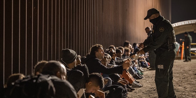 A U.S. Border Patrol agent checks for identification of immigrants as they wait to be processed by the U.S. Border Patrol after crossing the border from Mexico on December 30, 2022 in Yuma, Arizona. 