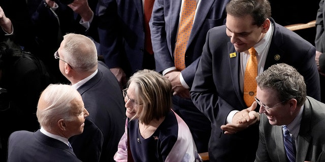 Senator AS George Santos (R-NY), kanan atas, menyaksikan Presiden Biden menyapa anggota Kongres setelah pidato kenegaraannya.  Dia telah didorong keluar dari kursi lorongnya sebelum Biden masuk.
