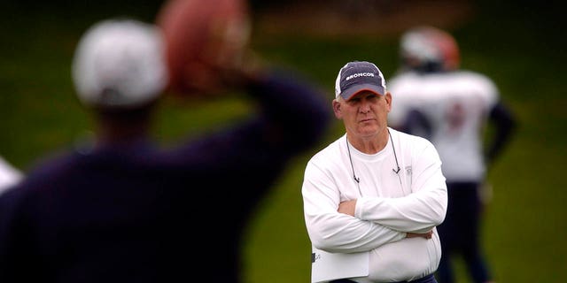 Broncos defensive coordinator Larry Coyer paces the field as players stretch out.