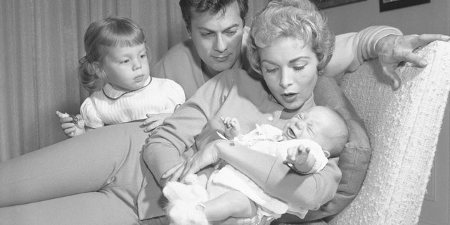 Janet Leigh holds Jamie Lee Curtis as a baby as Jamie's older sister Kelly, and dad, Tony Curtis, look on.