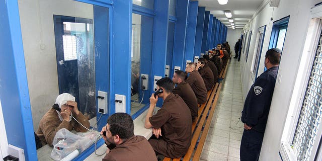 Palestinian men sitting in their brown prison uniforms behind glass talking on phones to relatives at the Gilboa Prison, east of the northern Israeli town of Afula. Most of the 850 adult male prisoners in this prison are serving very long jail terms and some are serving life sentences.