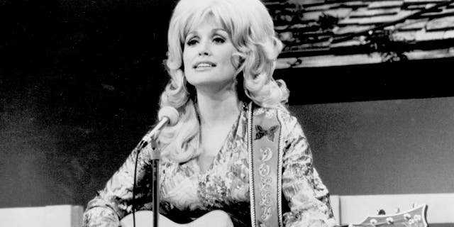 Country singer Dolly Parton performs onstage with an acoustic guitar in 1974. 