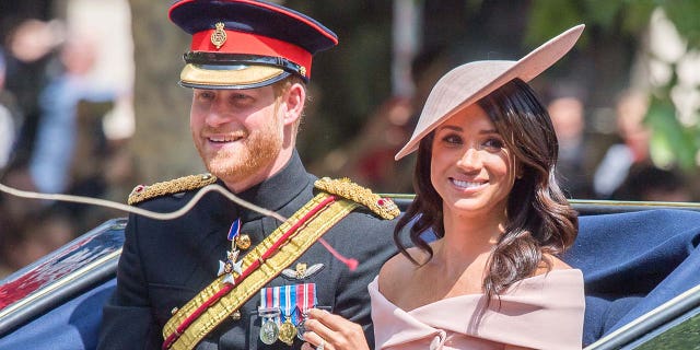 Prince Harry and Meghan Markle smile while riding in a carriage.