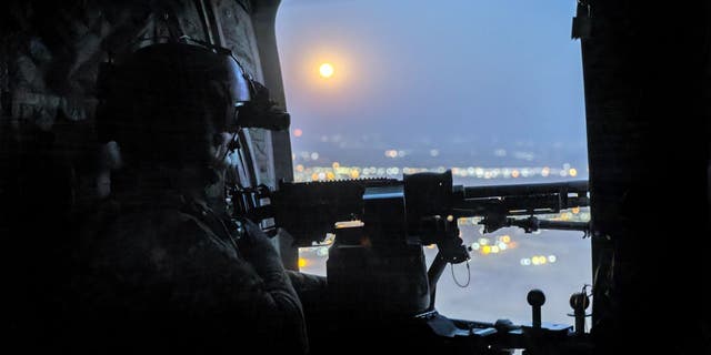 A "supermoon" shines as a U.S. Army CH-47 Chinook helicopter gunner scans the desert while transporting troops on May 26, 2021 over northeastern Syria.