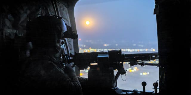 A "supermoon" shines as a U.S. Army CH-47 Chinook helicopter gunner scans the desert while transporting troops on May 26, 2021 over northeastern Syria.