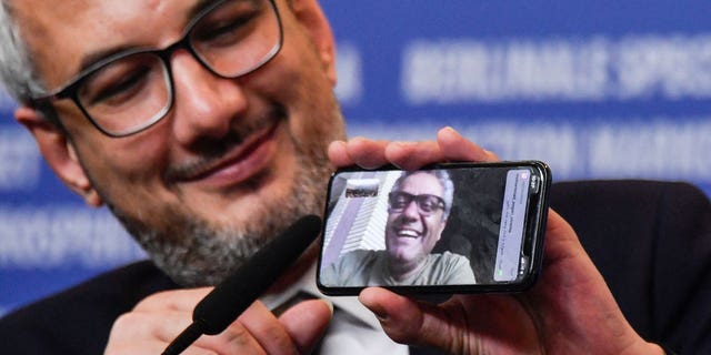 Iranian producer Farzad Pak is holding a phone showing Iranian director Mohammad Rasoulof receiving the "Golden Bear for Best Film" for his movie "There is no evil."