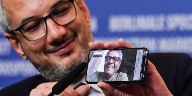 Iranian producer Farzad Pak holds a phone displaying Iranian director Mohammad Rasoulof who was awarded the "Golden Bear for Best Film" for his film "There is No Evil."