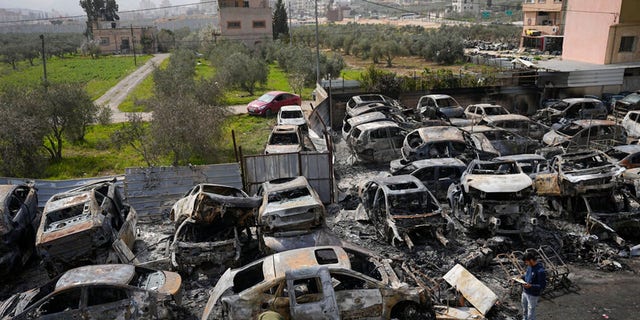 Palestinians inspect scorched cars in a scrapyard, in the town of Hawara, near the West Bank city of Nablus, Monday, Feb. 27, 2023.