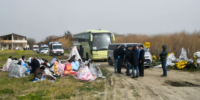 Rescued migrants covered in blankets, sit at a beach near Cutro, southern Italy, Sunday, Feb. 26, 2023.