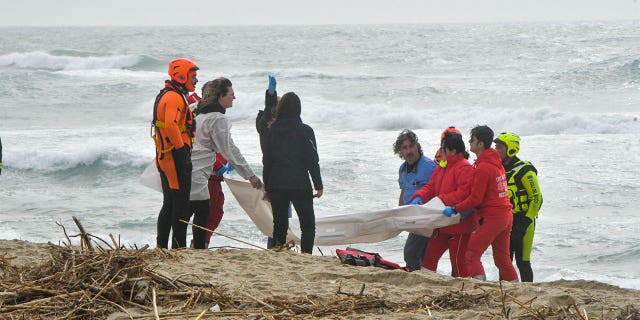 Rescuers recover a body after a migrant boat broke apart in rough seas, at a beach near Cutro, southern Italy, Sunday, Feb. 26, 2023. 