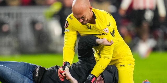 Marko Dmitrović of Sevilla FC fights with a spectator who ran onto the pitch during a UEFA Europa League knockout round playoff match between PSV and Sevilla FC at Philips Stadion on February 23, 2023 in Eindhoven, The Netherlands .