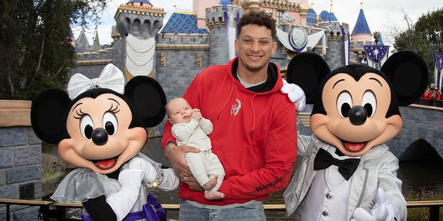 In this image provided by Disney, Patrick Mahomes of the Kansas City Chiefs and his newborn son, 11-week-old Bronze, pose with Mickey Mouse and Minnie Mouse in their shiny new outfits for The Walt Disney Company's 100th anniversary in Disneyland Park.  on February 13, 2023 in Anaheim, California.