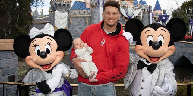 En esta imagen proporcionada por Disney, los jefes de Kansas City, Patrick Mahomes, y su recién nacido, Bronze, de 11 semanas, posan con Mickey Mouse y Minnie Mouse con sus brillantes atuendos nuevos para el 100.º aniversario de The Walt Disney Company en Disneyland Park el 13 de febrero de 2023. en Anaheim, California