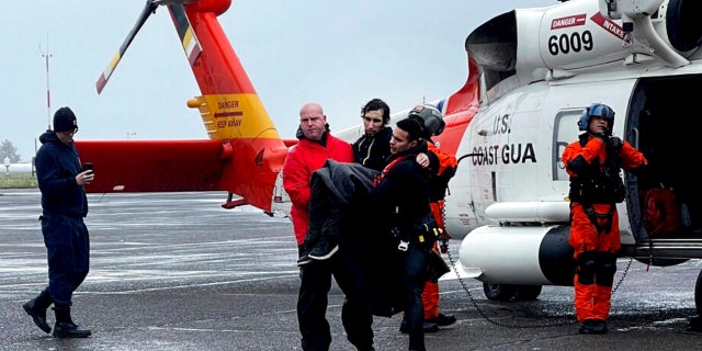 In this photo provided by the U.S Coast Guard Pacific Northwest, Coast Guard personnel help carry a swimmer from a rescue helicopter after he was rescued from the mouth of the Columbia River after his boat was capsized by a giant wave on Friday, Feb. 3, 2023, at Coast Guard Base Astoria, Oregon. 