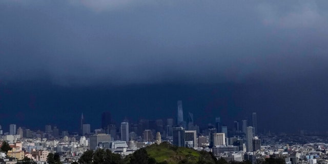Sun shines on Corona Heights, bottom, as the downtown skyline is obscured by rain clouds in San Francisco, Friday, Feb. 24, 2023. 