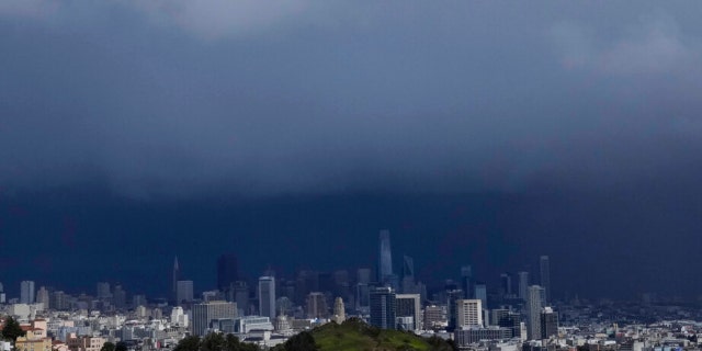 Sun shines on Corona Heights, bottom, as the downtown skyline is obscured by rain clouds in San Francisco, Friday, Feb. 24, 2023.