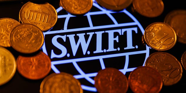 SWIFT (Society for Worldwide Interbank Financial Telecommunication) logo displayed on a phone screen and coins are seen in this illustration photo taken in Krakow, Poland on January 23, 2022.