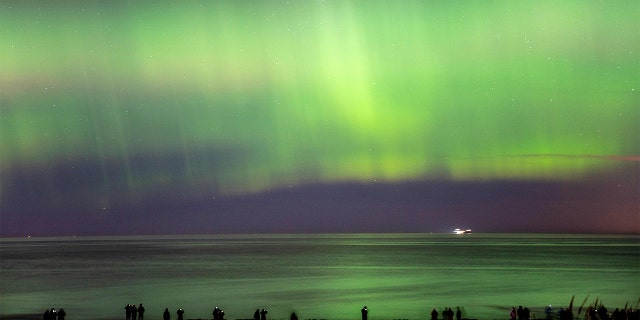Cahaya utara (aurora borealis) menerangi langit saat pengunjung berjalan di sepanjang Pantai Hornbaek di bagian utara Sealand, Denmark, pada 27 Februari 2023.