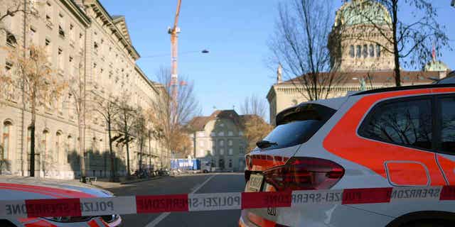 Police vehicles are parked in front of the Swiss Parliament after a man wearing a bulletproof vest was found near the entrance of the building with explosives.