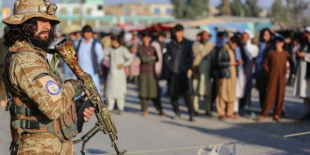 A Taliban security member stands guard as Afghan people wait to cross into Pakistan at the Torkham border crossing between Afghanistan and Pakistan, in Nangarhar province, on Feb. 23.