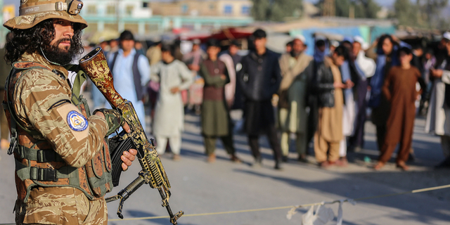 A Taliban security member stands guard as Afghan people wait to cross into Pakistan at the Torkham border crossing between Afghanistan and Pakistan, in Nangarhar province, on Feb. 23.