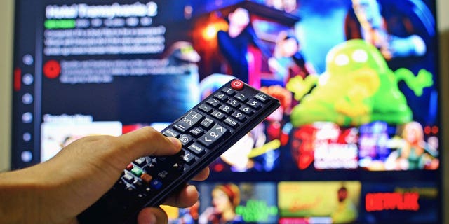 A hand holding up a remote to select something to watch on Netflix.