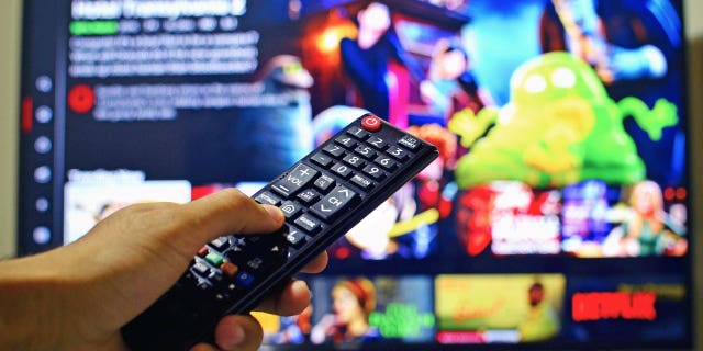 A hand holding a remote control to choose what to watch on Netflix.