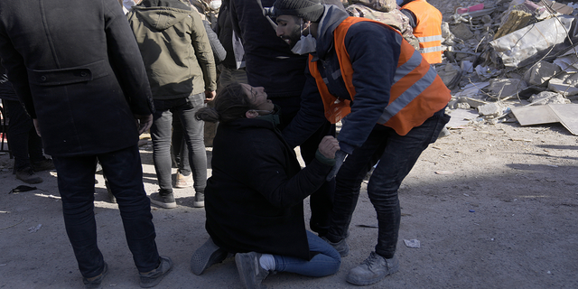 Seorang wanita menangis saat orang-orang berdiri di depan sebuah bangunan yang hancur di Kahramanmaras, tenggara Turki, pada Senin, 13 Februari.