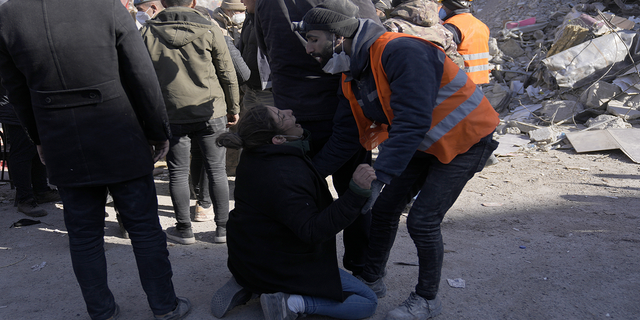 A woman cries as people stand in front of a destroyed building in Kahramanmaras, southeastern Turkey, on Monday, Feb. 13.