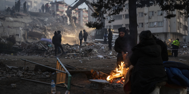 People warm around a fire as rescuers search in a destroyed building in Kahramanmaras, southeastern Turkey, on Thursday, Feb. 9.