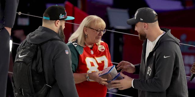 Mother Donna Kelce (C) gives cookies to Jason Kelce (L) #62 of the Philadelphia Eagles and Travis Kelce (R) #87 of the Kansas City Chiefs from her son during opening night of Super Bowl LVII presented by Fast Twitch at the Footprint Center on February 06, 2023, in Phoenix, Arizona.