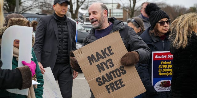 Man holds cardboard sign that says "Make NY3 Santos free" during caravan