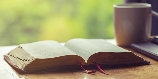 open Bible on table next to coffee mug by window